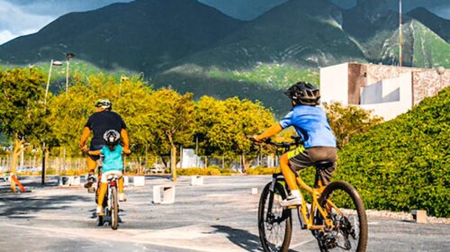 imagem mostra um homem e duas crianças andando de bicicleta em um espaço aberto